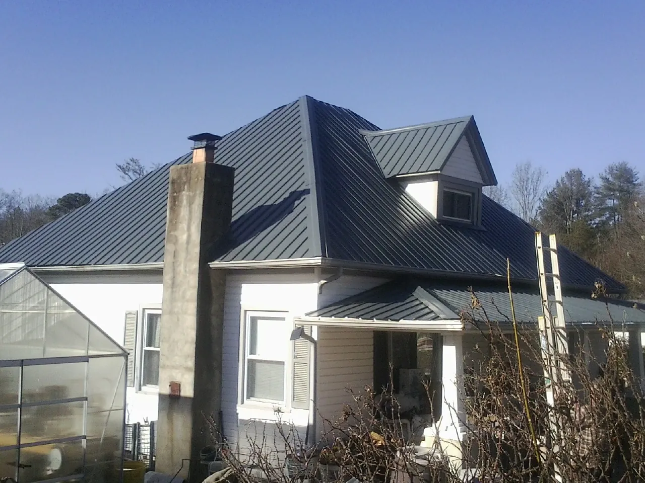 Dark blue standing seam metal roof on a white farmhouse with dormer — Slate & Tile Roof Repair by Roofing Brothers in Gwinner