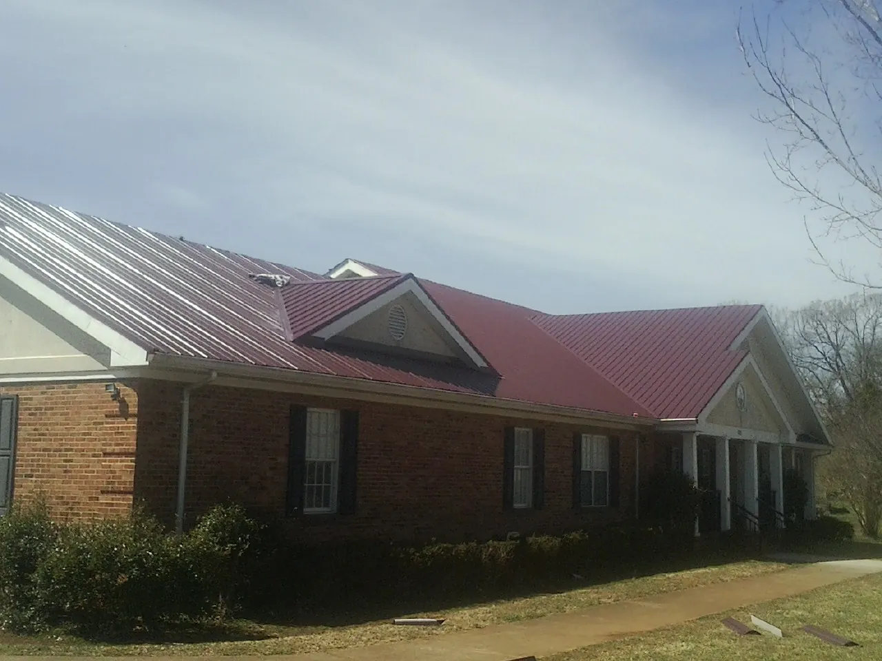 Red metal roof with gabled entries on a long brick building, from a Hail Damage Roof Repair job in Gwinner