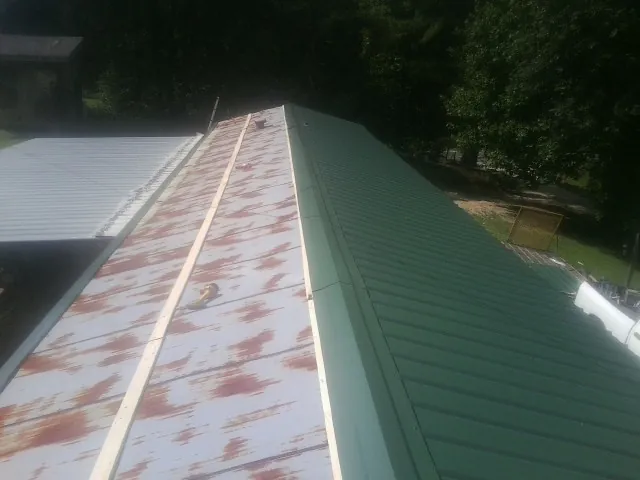 Old rusted panels beside newly installed green metal roofing — Wind Damage Roof Repair by Roofing Brothers in Gwinner