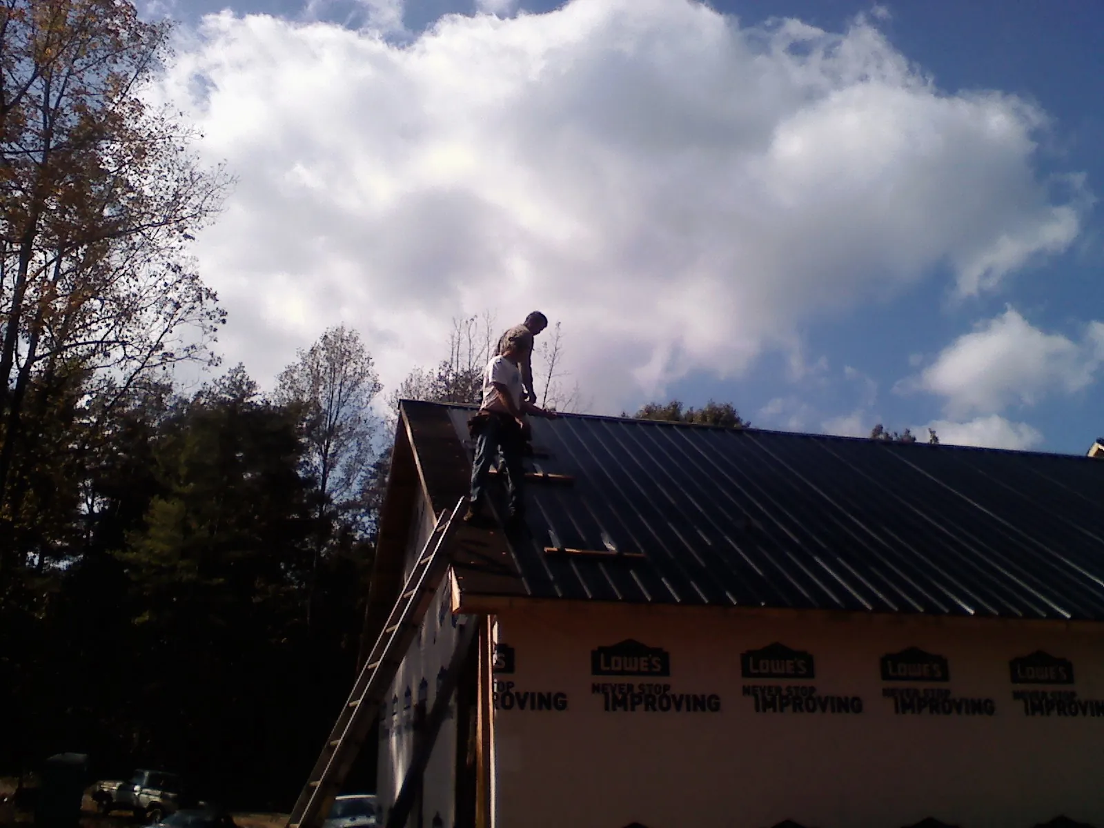 Roofer fastening dark metal panels high against a cloudy sky, from a Roof Inspection job in Gwinner