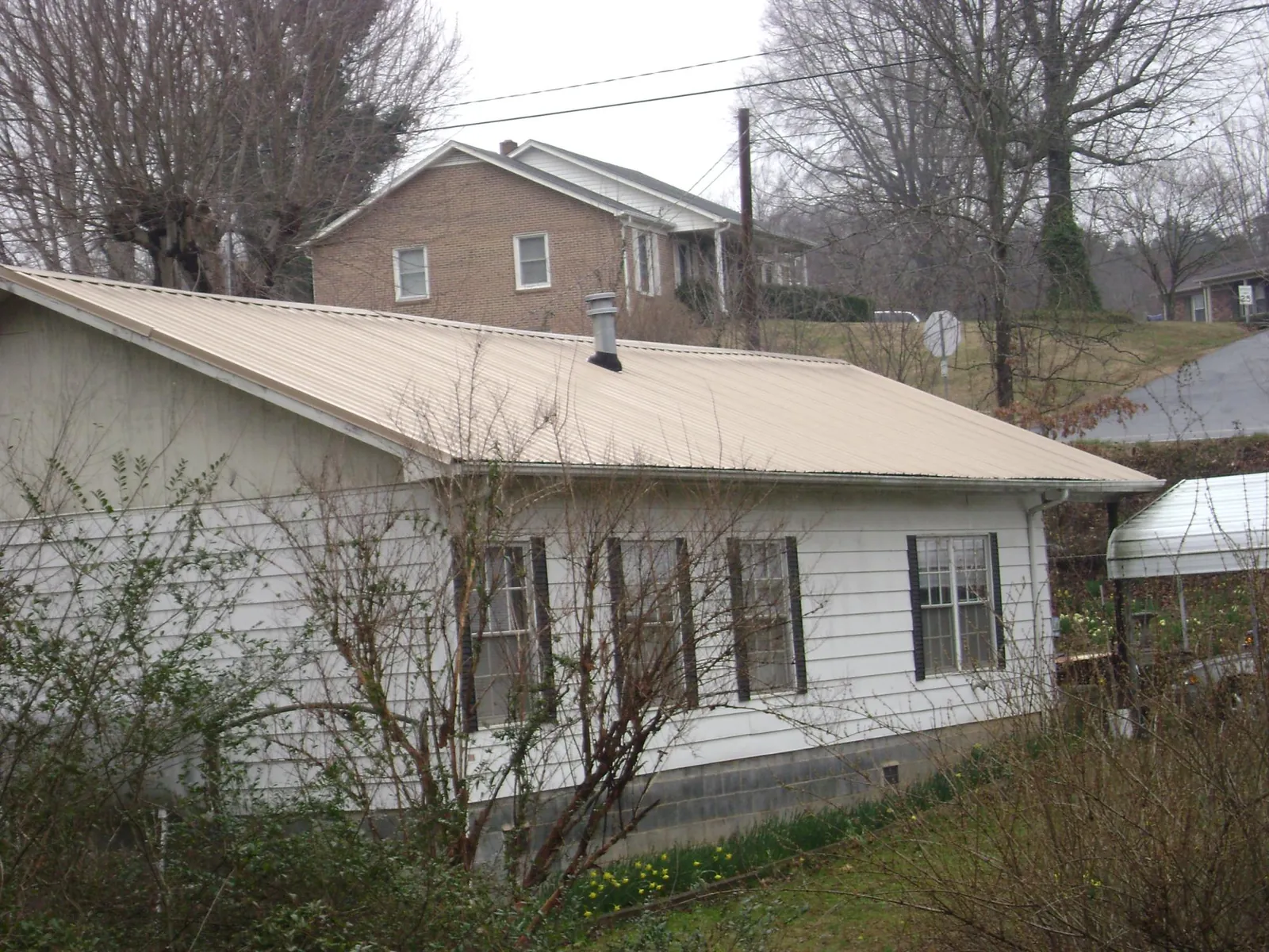 Tan metal roof on a white sided house set into a hillside — Commercial Roofing by Roofing Brothers in Gwinner